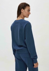 Felpa blu navy con scollatura a girocollo, polsini e orlo a costine. Presenta una texture morbida e maniche raglan. Abbinata a pantaloni coordinati.