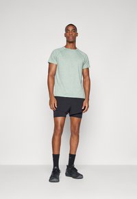 Camiseta atlética de manga corta en verde jaspeado, pantalones cortos negros, zapatillas negras y calcetines. Diseño simple con mangas raglán y tela transpirable.