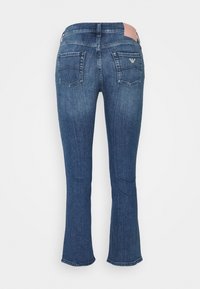 Blå denimbyxor med flare-modell, med medelhög midja, två bakfickor och en kontrasterande rosa läderpatch på midjebandet.