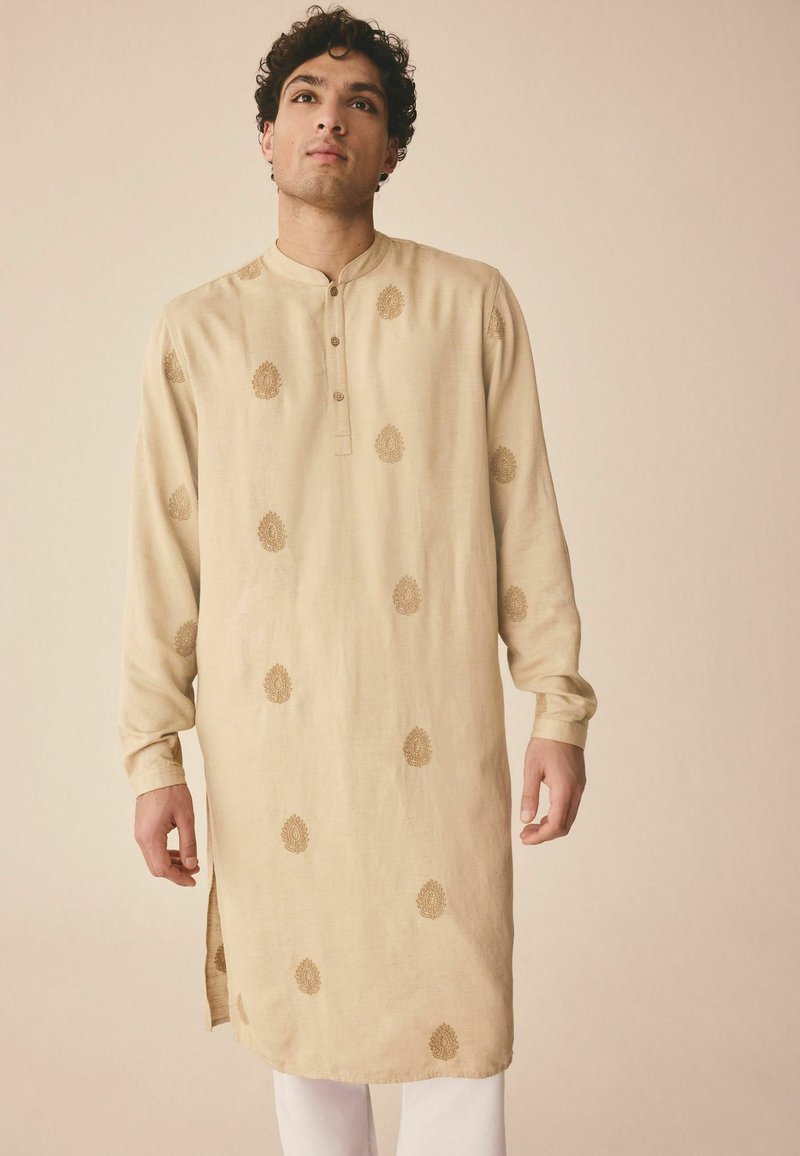 Beiger Kurta mit langen Ärmeln, Knopfleiste und goldenen Blattmustern throughout. Seitenschlitze verbessern die Beweglichkeit. Glatte Stoffoberfläche.