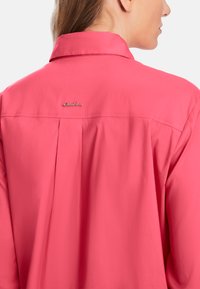 Pink shirt with a collar, featuring a small metallic logo on the back, pleat detail, and smooth fabric texture.