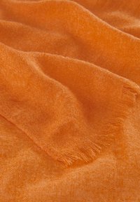 Tissu orange au toucher doux et à la légère brillance, avec des bords frangés et des plis doucement drapés. Idéal pour des écharpes ou des capas.