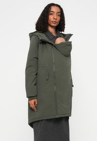 Oliven grøn parka med hætte, lynlås lukning og frontlomme til at bære en baby. Har justerbare snøringer og blødt stof.
