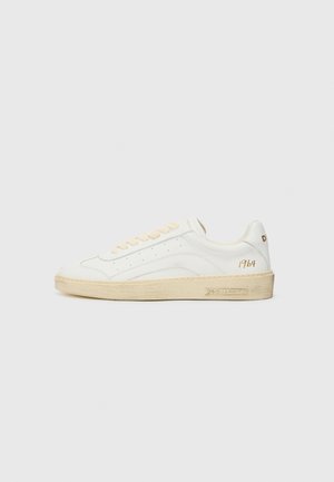 Baskets en cuir blanc avec lacets beiges, semelle en caoutchouc blanc cassé et perforations subtiles. Présente un texte doré "1964" et un logo à l'arrière.