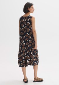 Sleeveless, navy dress with large brown and beige circle pattern, ruffled hem, and back keyhole detail. Paired with brown sandals.