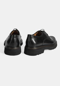 Chaussures en cuir noir avec une finition lisse, bout arrondi, semelle en caoutchouc épaisse et surpiqûre décorative le long de la semelle intermédiaire. Design à lacets à l'avant.