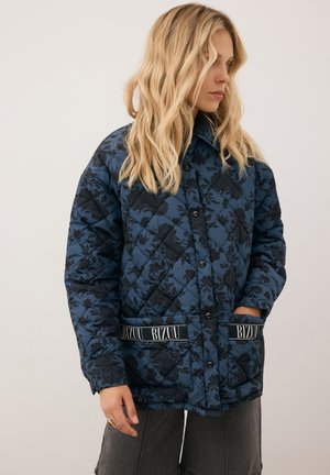Gequilted blauwe jas met een donker bloemig patroon, voorzien van knoopsluiting, twee voorzakken met logo-accenten en een hoge kraag.