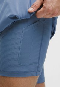 Pantalones cortos deportivos azules hechos de una tela texturizada y transpirable, con un bolsillo lateral y una cintura elástica, mostrando un detalle en primer plano.