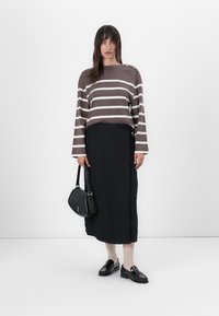 Brun og hvit stripete genser med lange ermer, svart skjørt, svart veske, svarte loafers og beige sokker. Detaljerte skulderknapper synlige.