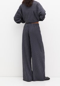 Granatowy, pasiasty zestaw ubrań o luźnym kroju, składający się z koszuli z kołnierzykiem i spodni w szerokim kroju, wykonanych z lekkiego materiału. Akcentowany paskiem.