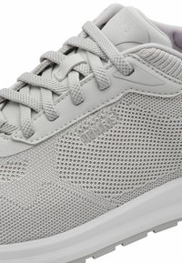 Baskets sportives gris clair avec une tige en maille respirante, des lacets plats et un design texturé, dotées d'une semelle blanche rembourrée et d'un logo distinctif.