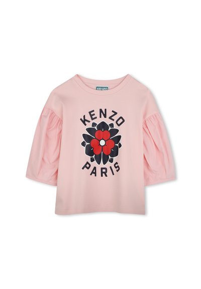 T-shirt rose à manches courtes avec des manches bouffantes, présentant un grand motif floral en rouge, noir et blanc, le texte "KENZO PARIS" en dessous de la conception.