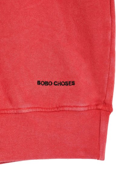 Section de tissu rouge d'un vêtement avec un poignet côtelé et "BOBO CHOSES" brodé en petites lettres noires.