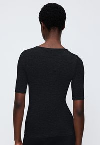 T-shirt noir à manches courtes avec une texture douce et une coupe ajustée, présentant un décolleté large et un dos sans couture.