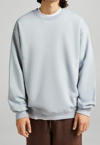 Lichtblauwe sweatshirt met een ronde hals en verlaagde schouders. Beschikt over ribbelboorden en een ribbelzoom, met subtiele branding op de voorkant.