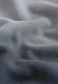 Țesătură gri texturată cu o ușoară strălucire, având o suprafață netedă și valuri blânde, prezentând un model de tricotaj uniform.