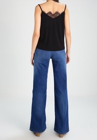 Camisole noire avec détail en dentelle au dos, associée à un jean bleu taille haute, jambes larges. Tissu lisse, coupe ample et denim délavé clair.