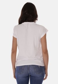 T-shirt bianco a maniche corte con scollatura rotonda e vestibilità rilassata, indossato da un modello di spalle, abbinato a un paio di jeans in denim blu.