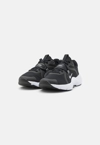 Zwarte sportieve schoenen met een bovenkant van mesh, gestructureerde details, witte tussenzool en zwarte buitenzool. Nike-logo zichtbaar aan de zijkant.