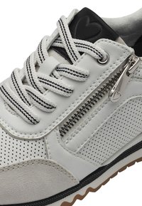 Baskets en cuir blanc avec des accents en daim texturé, un détail de fermeture éclair argenté et des lacets noirs avec des rayures blanches. Panneaux latéraux perforés.
