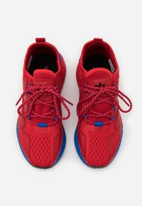 Czerwone buty sportowe z przewiewną siateczką, teksturowanym wzorem, niebieskimi akcentami i wzorzystymi czerwonymi sznurowadłami. Płaska, czarna gumowa podeszwa.