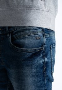 Granatowe dżinsy o teksturowanym wykończeniu, z pięcioma kieszeniami i małą metką marki na tylnej kieszeni.