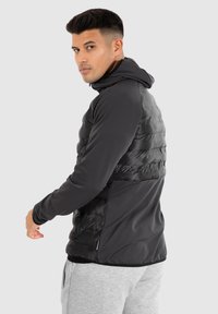 Schwarze isolierte Jacke mit Kapuze, die ein schlankes Design und eine Kombination aus strukturierten und glatten Stoffpanelen aufweist.
