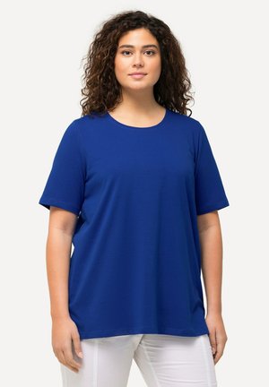T-shirt bleu à manches courtes en tissu doux avec un col rond. Coupe ample et design simple, associé à un pantalon blanc.