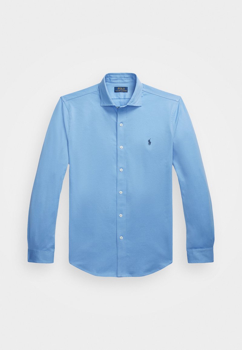 Lys blå langermet skjort med knapper laget av bomull. Har en klassisk krage og en liten logo brodert på venstre bryst.