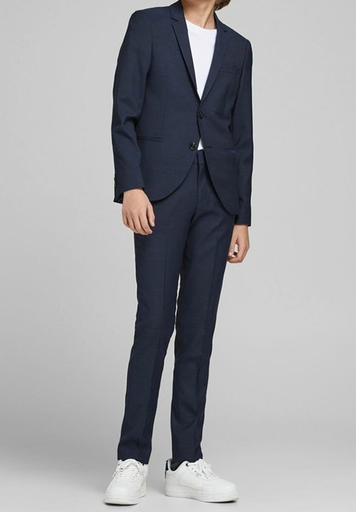 Abito blu navy a taglio slim, con blazer monopetto, rever a lancia e pantaloni coordinati. Indossato con t-shirt bianca e sneakers.