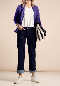 Fioletowa marynarka, biała koszulka, ciemne dżinsy z podwiniętymi nogawkami i białe trampki. Torba płócienna w czarno-białe paski.