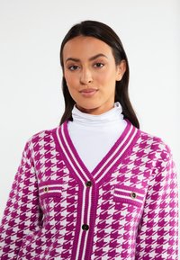 Lila och vit houndstooth-kardigan med V-ringning, två bröstfickor och stora knappar. Inkluderar kontrasterande ribbade detaljer.