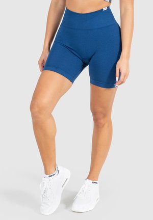 Blauwe hooggewaisted sportshorts van rekbare, gestructureerde stof, die net boven de knie eindigen. Gekleed met witte sneakers.