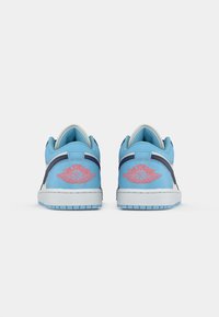 Zemu un baltu sporta apavu pāris ar tumši zilo akcentu, attēlots no aizmugures, ar sarkaniem Air Jordan logo uz papēžiem.