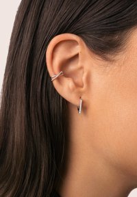 Orecchini a cerchio in argento presentano un design intrecciato con un accento scintillante. Gli orecchini sono attaccati al lobo, evidenziando la loro finitura lucida.