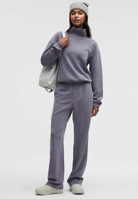 Violetti oloasusetti, joka sisältää korkeakauluksisen collegepaidan ja siihen sopivat housut. Sileä pinta, rento istuvuus ja yksinkertainen muotoilu. Vaaleanharmaat jalkineet.