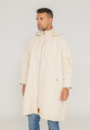 Beige langer Mantel mit hohem Kragen, großem Reißverschluss vorne und seitlichen Taschen. Das Material ist glatt mit einem leicht glänzenden Finish.