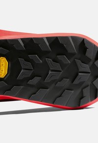 Czarna gumowa podeszwa z agresywnym wzorem bieżnika, z żółtym logo Vibram i czerwonym akcentem wzdłuż krawędzi.