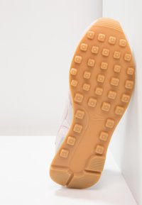 Semelle de chaussure avec des crampons en caoutchouc beige et le logo Nike, vue par le dessous sur fond blanc.