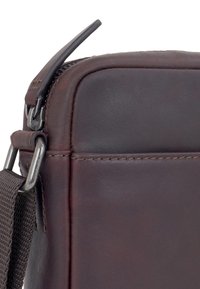 Angolo di borsa in pelle marrone con chiusura a zip, accessori in argento e tracolla in tessuto testurizzato. Superficie liscia con dettagli di cucitura precisi.