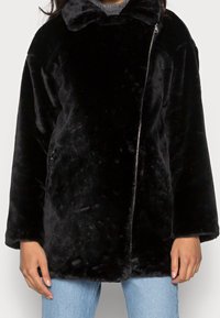 Chaqueta de pelo sintético negra con una textura suave, que cuenta con un cierre de cremallera, cuello ancho y mangas largas. El diseño es de corte holgado y relajado.