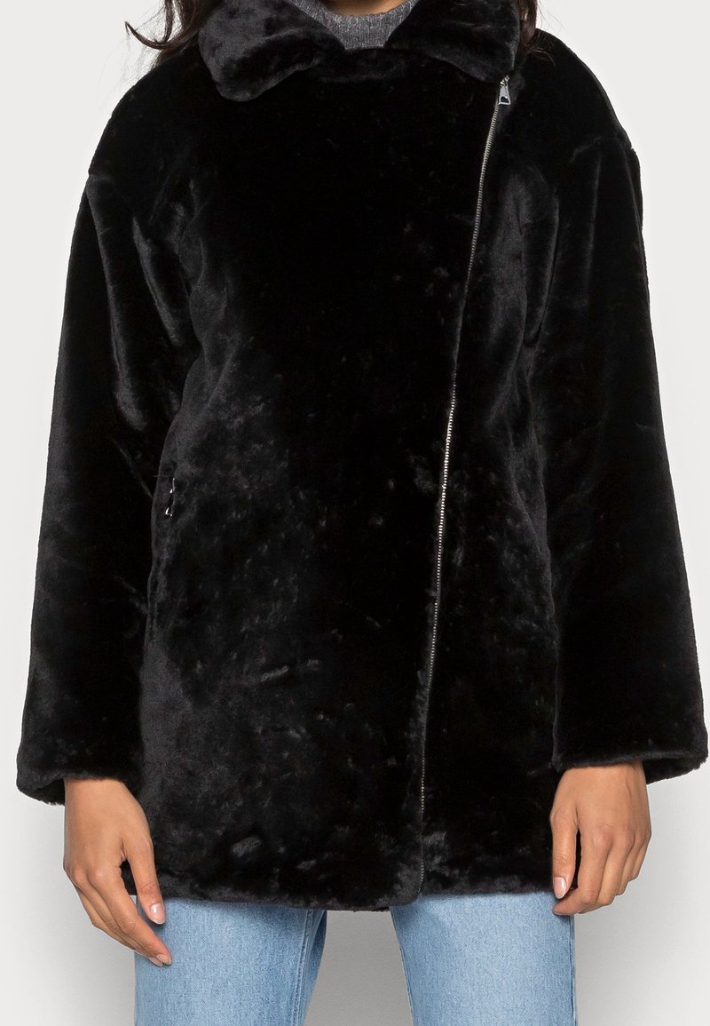 Chaqueta de pelo sintético negra con una textura suave, que cuenta con un cierre de cremallera, cuello ancho y mangas largas. El diseño es de corte holgado y relajado.