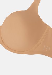 Lys beige polstret bh med glat stof, formede skåle, justerbare stropper og et logo-detalje på siden. Blødt, sømløst design.