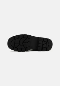 Semelle de chaussure en caoutchouc noir avec des motifs de bande de roulement profonds et une surface texturée. Caractérisée par un design rectangulaire et angulaire pour une adhérence et un soutien.