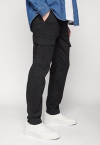Pantaloni cargo negri din bumbac, cu buzunare laterale, o croială confortabilă, asortați cu adidași albi și o cămașă din denim.