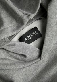 Lähikuva taitellusta harmaasta kankaasta, jonka sisäpuolella on musta vaatemerkki, jossa lukee "aprel".