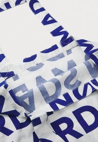 Einschlag aus Baumwolle mit weißem Grund, kräftigen blauen Buchstaben und einem grafischen Muster. Verstellbare Träger und saubere Nahtdetails.