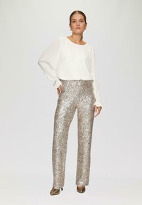 Witte, lange mouwen blouse met een geplooide halslijn, gecombineerd met een hoge taille, glinsterende zilveren sequinbroek en gouden hakken.