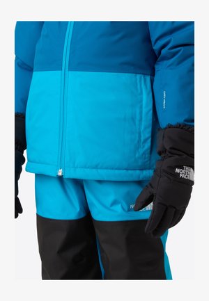 Blå og sort skijakke og bukser med en struktureret finish. Har lynlås, justerbare manchetter og logoaccents.