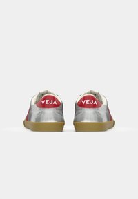 Silver sneakers with red accents and a gum sole. Features a textured finish, white laces, and branding on the heel.
